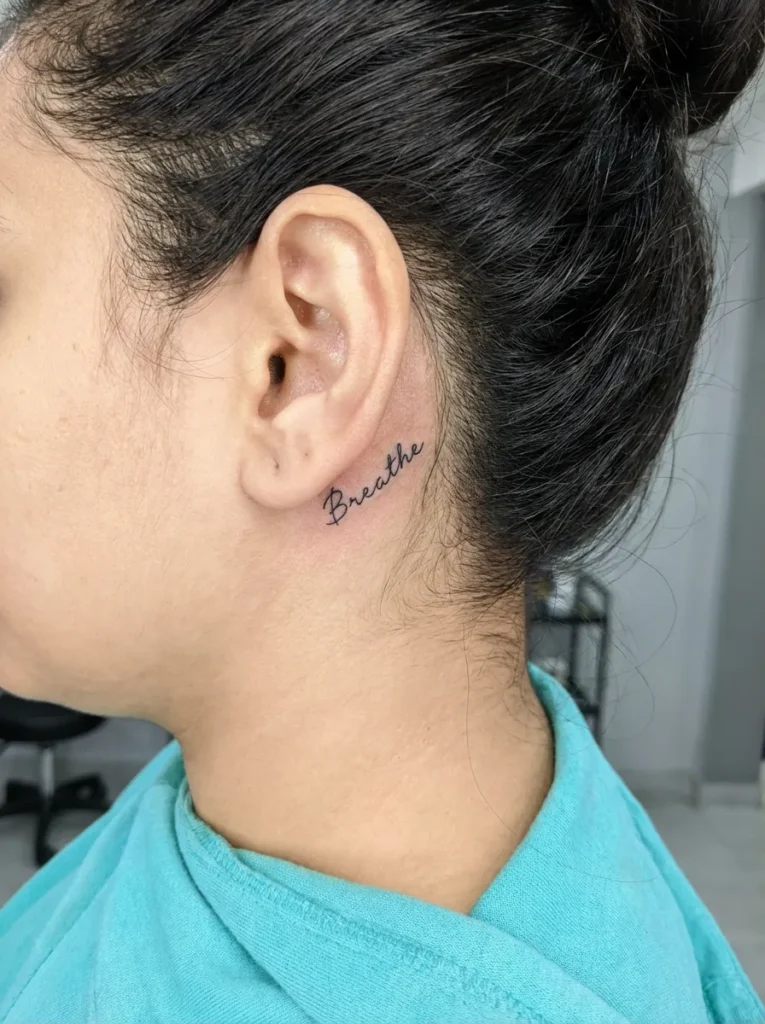 Tiny Script Word Behind Ear Tattoo